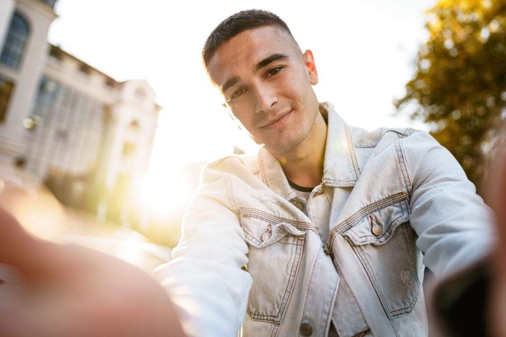 Portrait of young man taking a selfie while out on the city street, close up